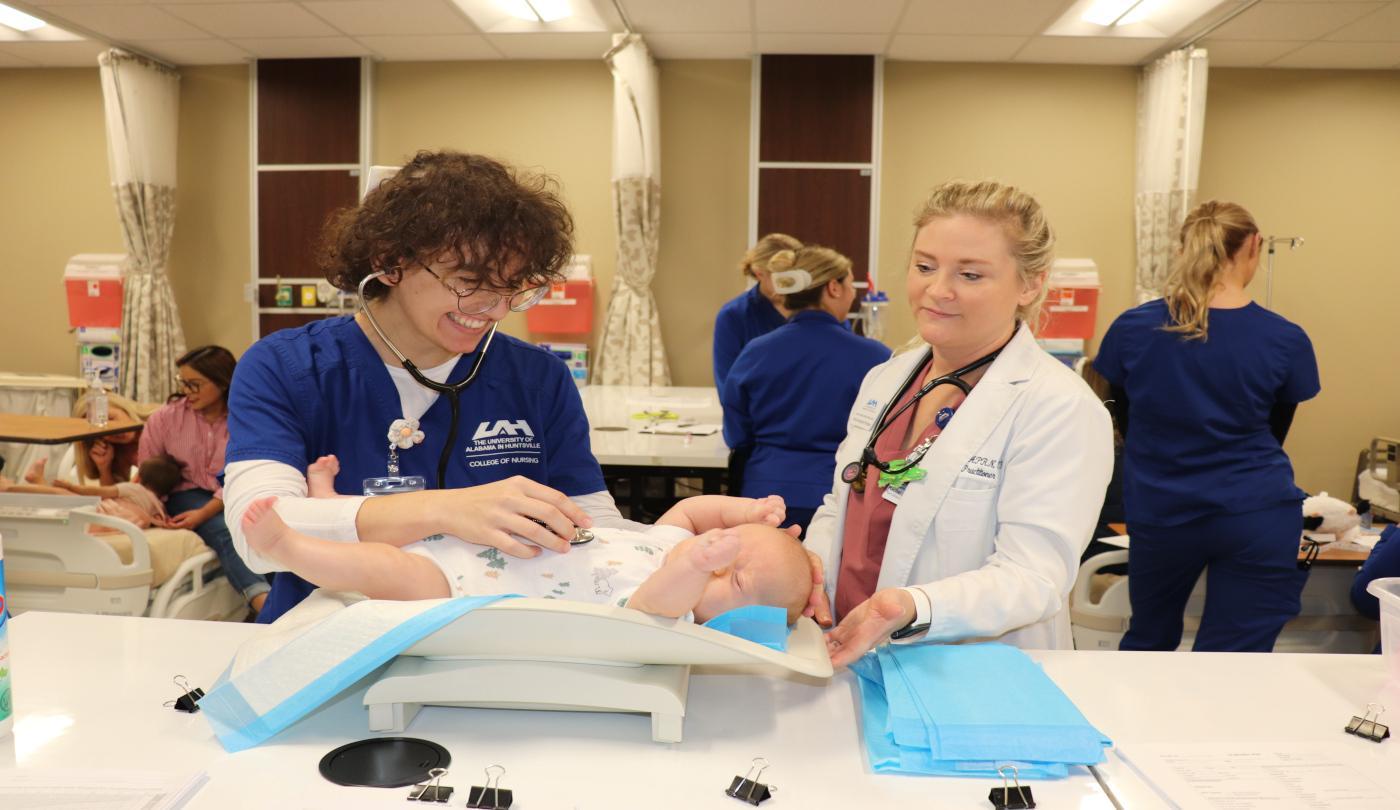 A student practices listening to an infant's heart during a pediatric health assessment while an instructor looks on. ABSN-NUR-4017