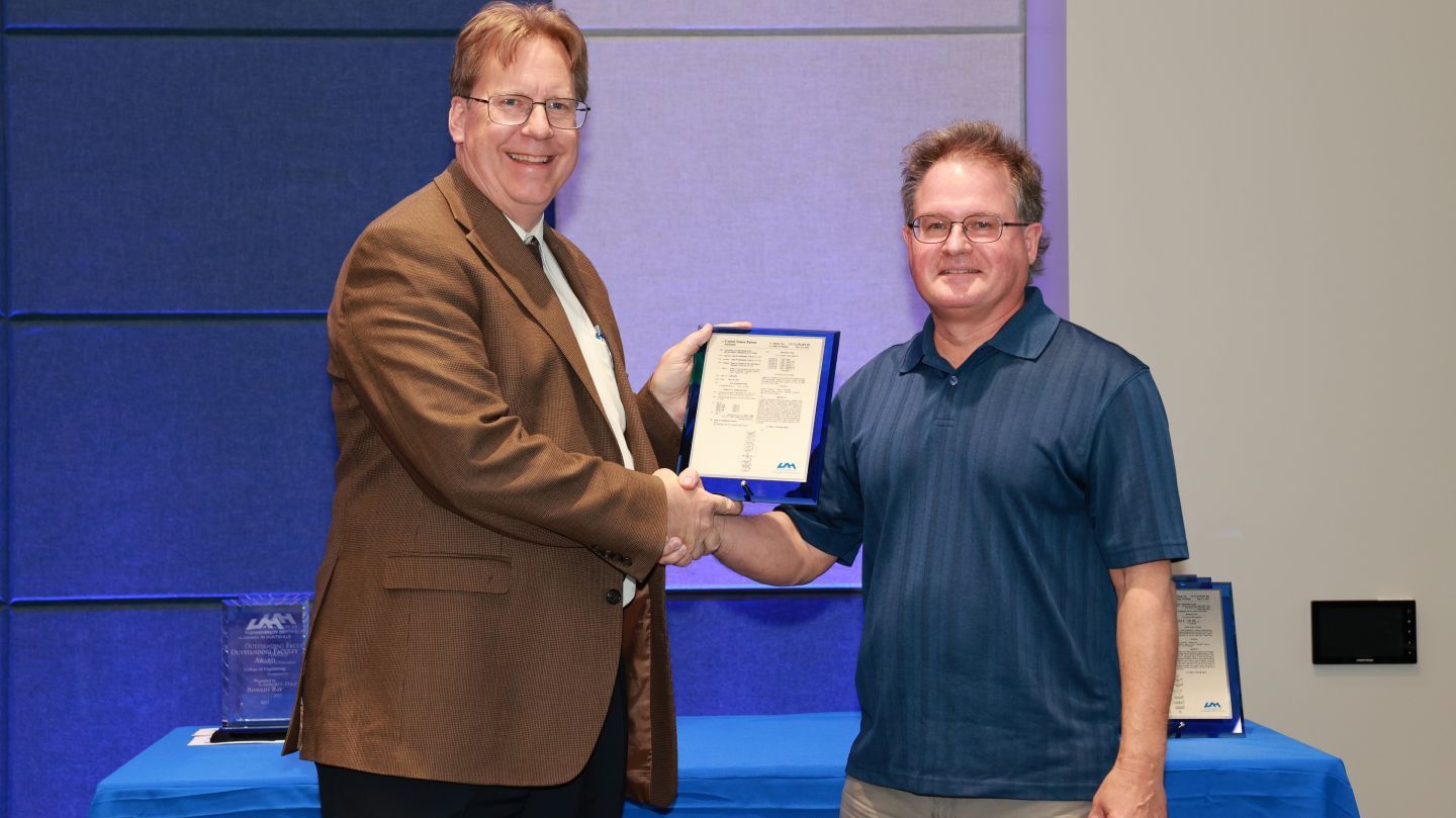 Dr. Robert Lindquist shaking hands and presenting a plaque to Dr. John Mecikalski