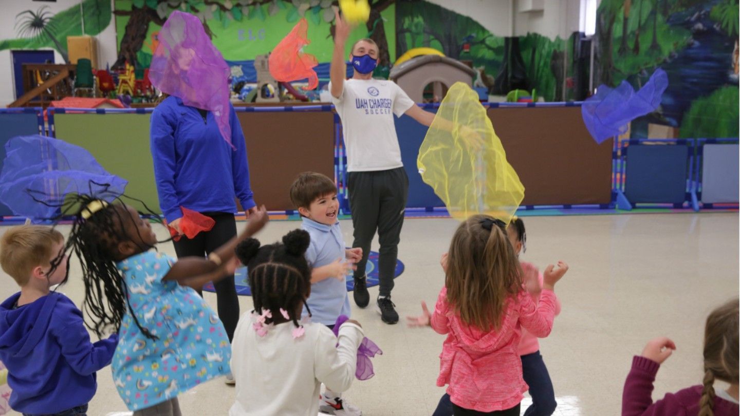 Physical education students throw cloths in the air with excited children children 