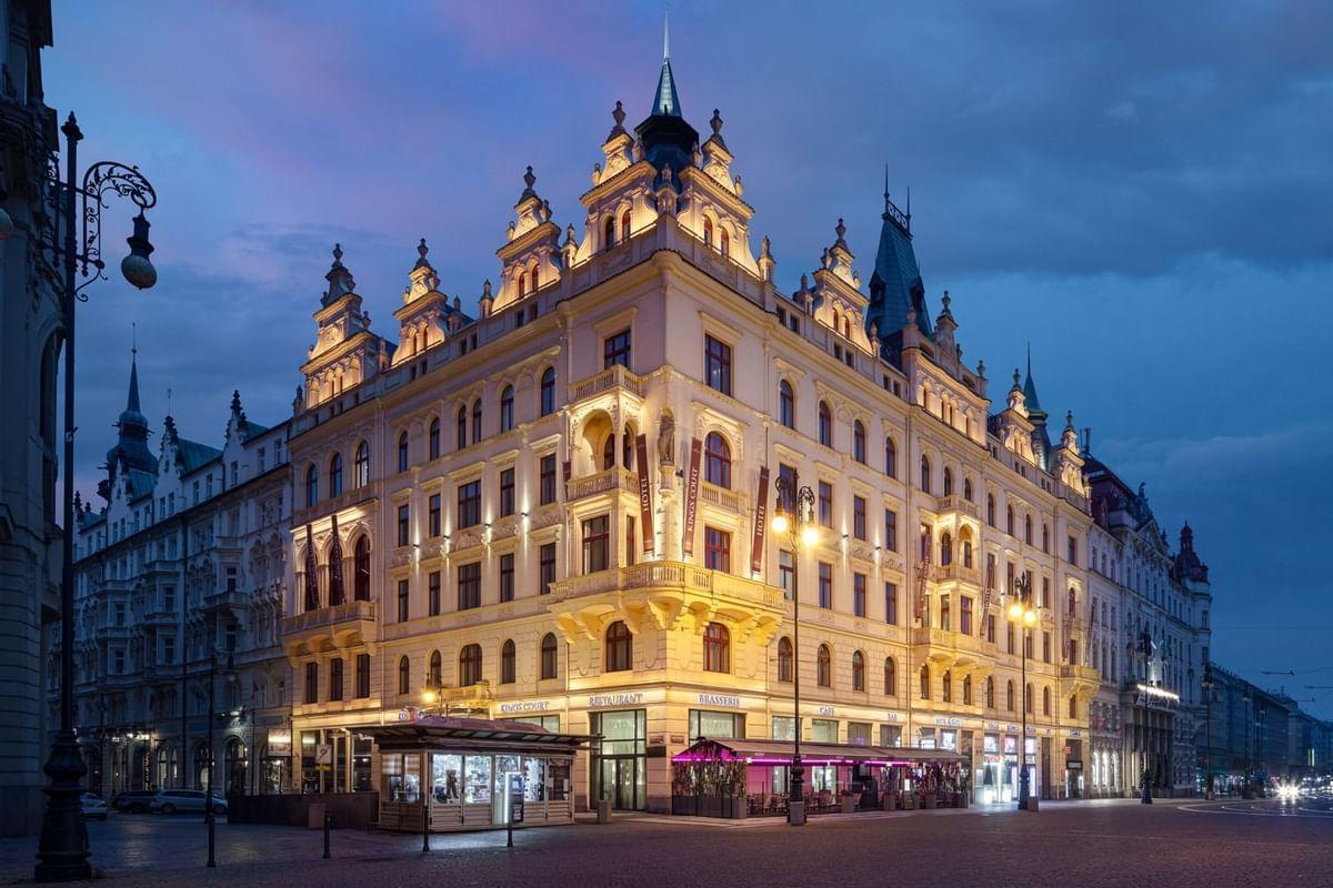 Illuminated Hotel Kings Court building at dusk, showing its ornate facade on a Prague street corner.
