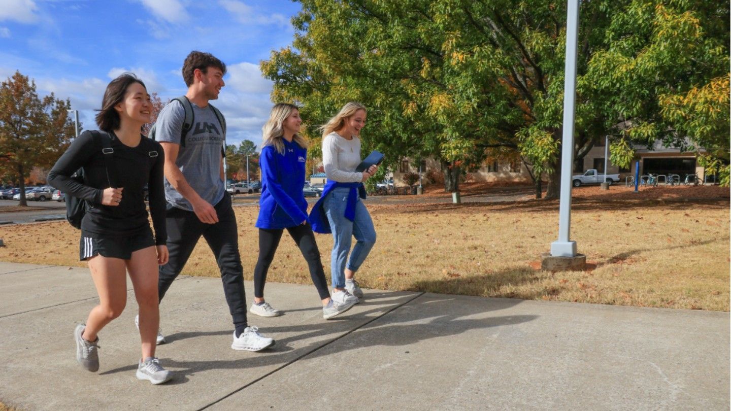 four students walk side by side down a sidewalk