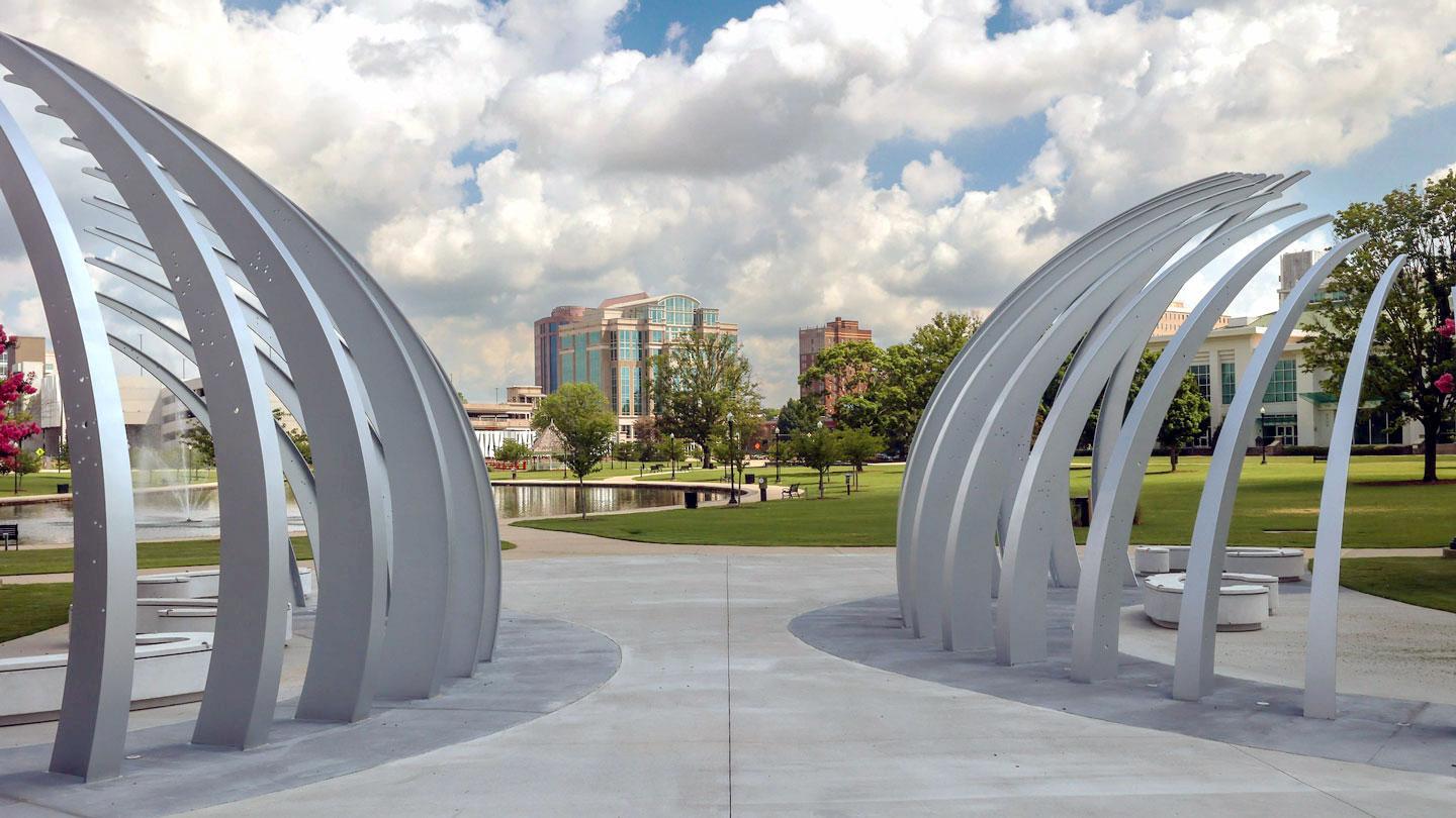 Looking through a large ribbed statue into Big Spring Park in Huntsville on a summer day