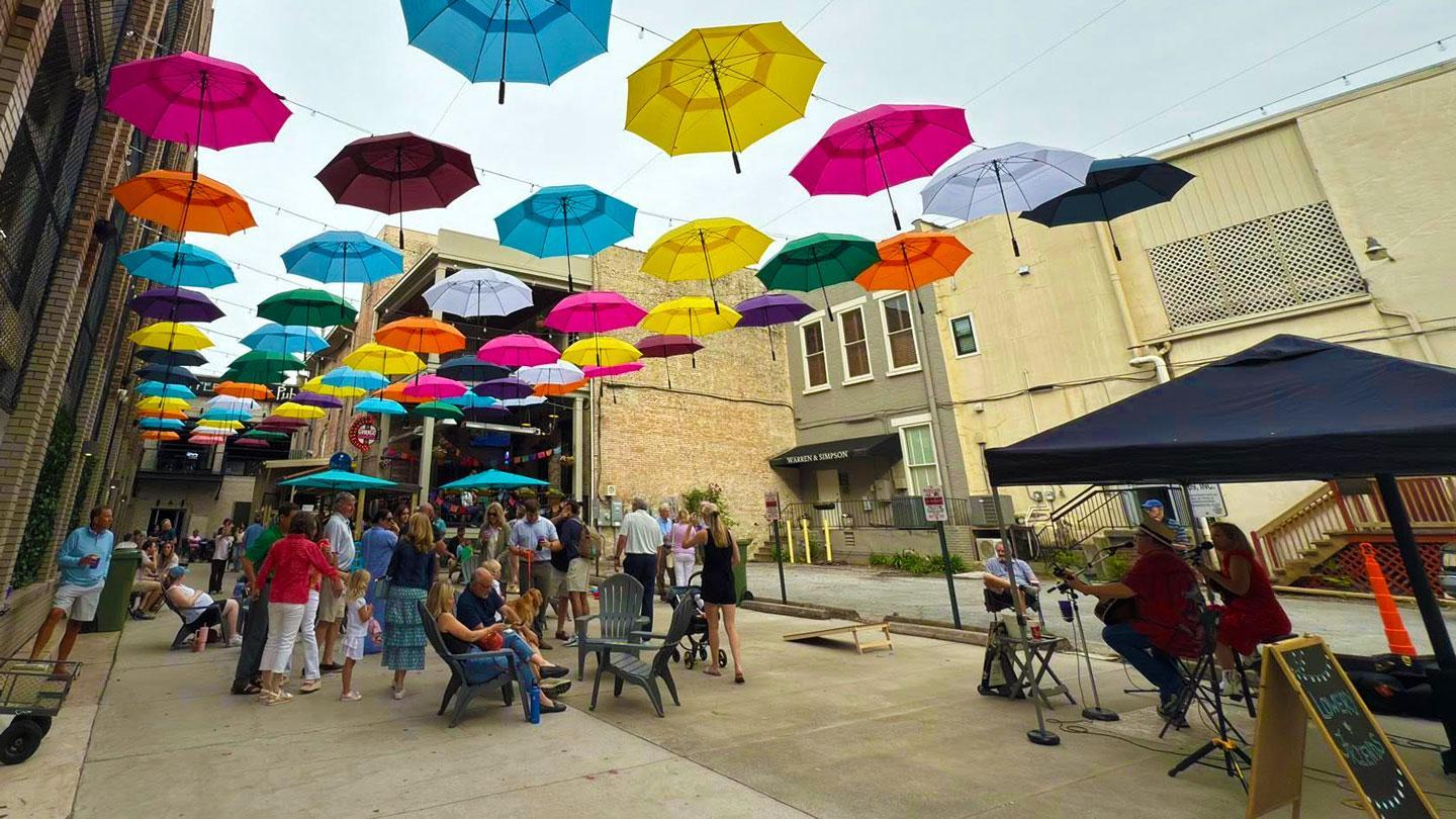 A canopy of colorful floating umbrellas shade a public patio full of people in downtown Huntsville.