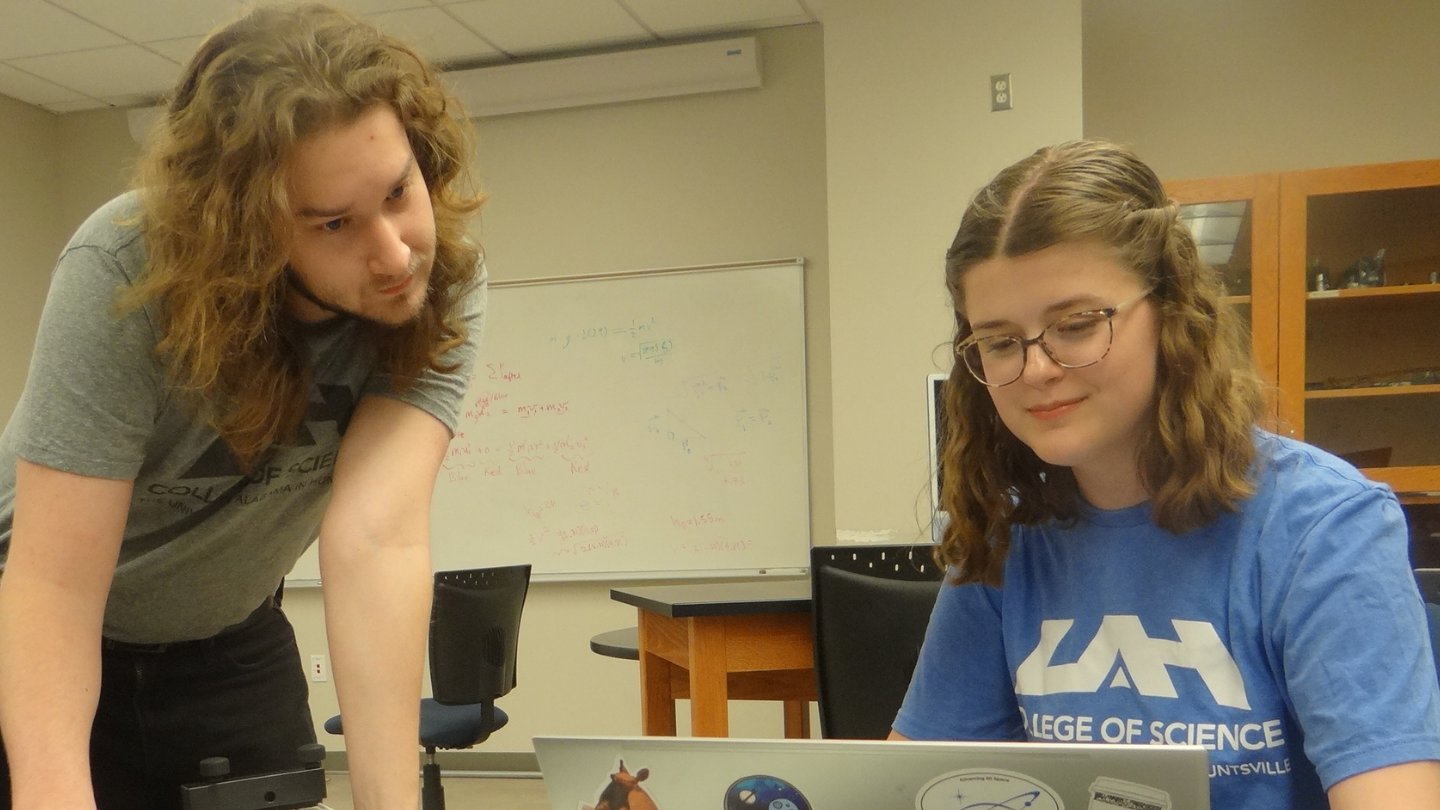 Two UAH Computer Science students collaborate using a laptop in a classroom.
