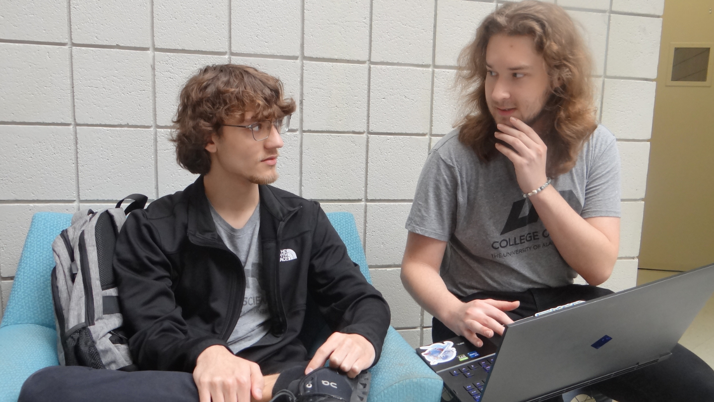Two Computer Science students at UAH collaborate on a laptop in a campus study area.