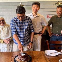 friends gathered around a table cutting celebration cake