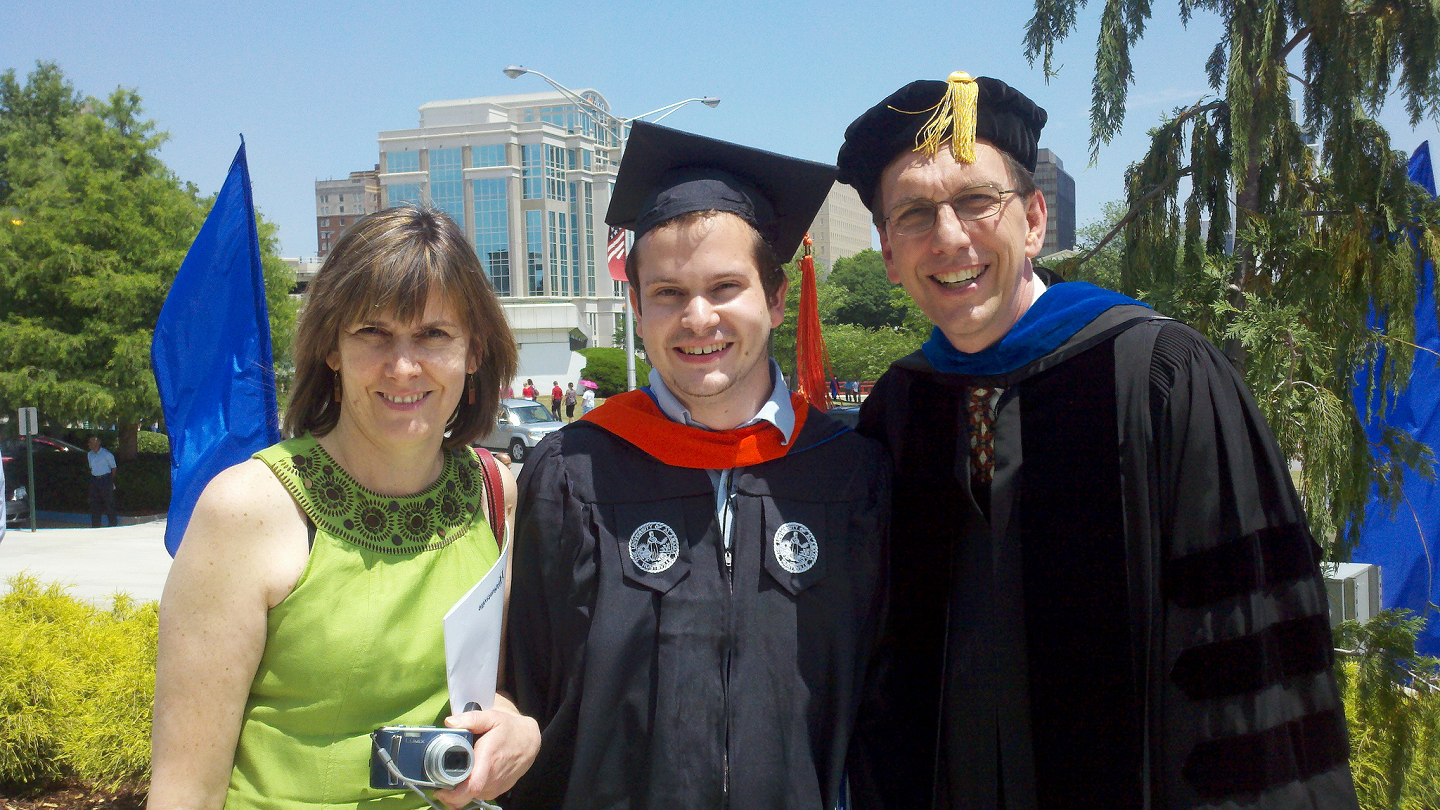 two people in graduation attire stand next to a woman in a dress