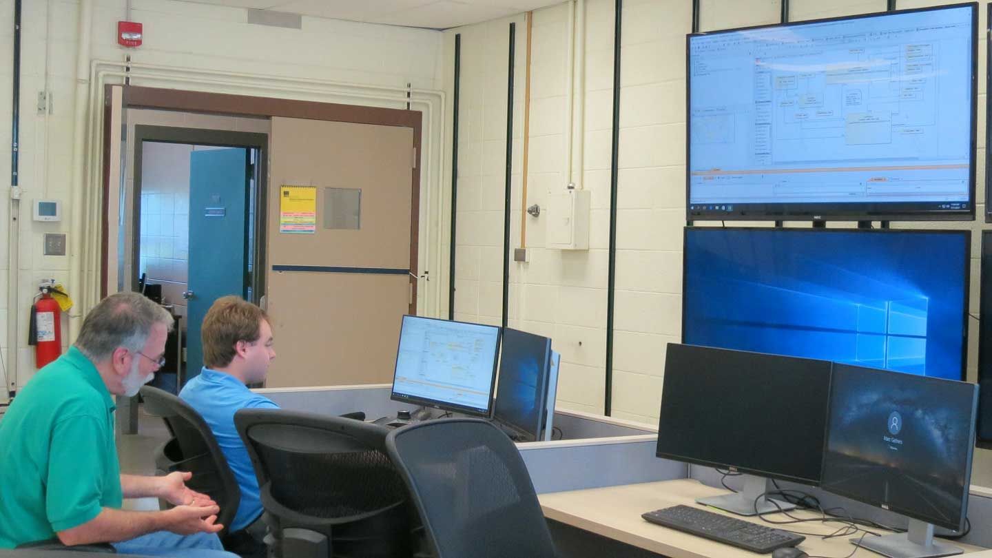 two men examine many screens