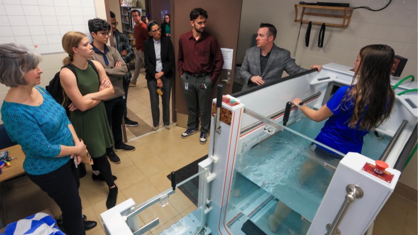 Kinesiology students stand together observing a large water bath