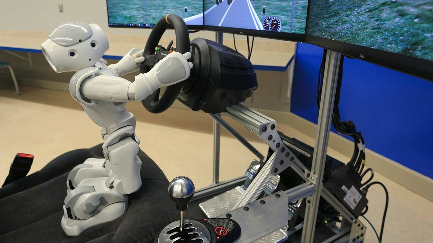 a robot uses a steering wheel to operate a driving simulator