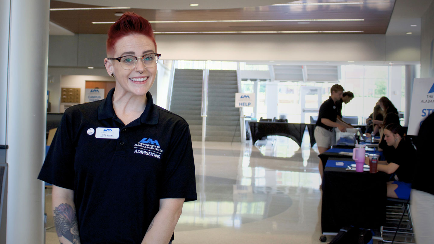 Katie Greene welcoming as an admissions representative stands in a modern lobby filled with information tables and bright, open spaces.