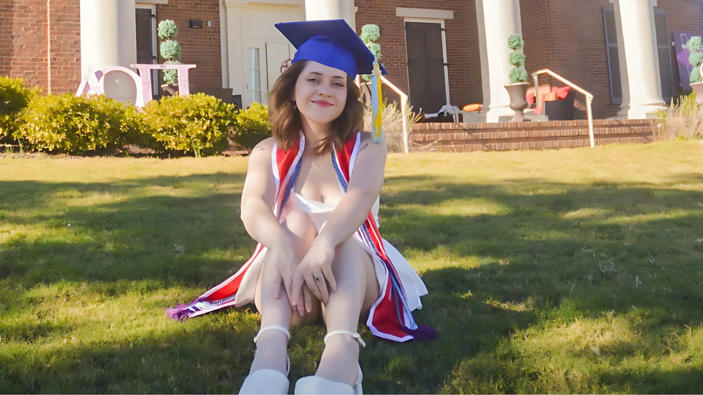 A photo of Shelby Cave in graduation attire sits on a grassy lawn, posing in front of a brick building with decorative plants and letters.