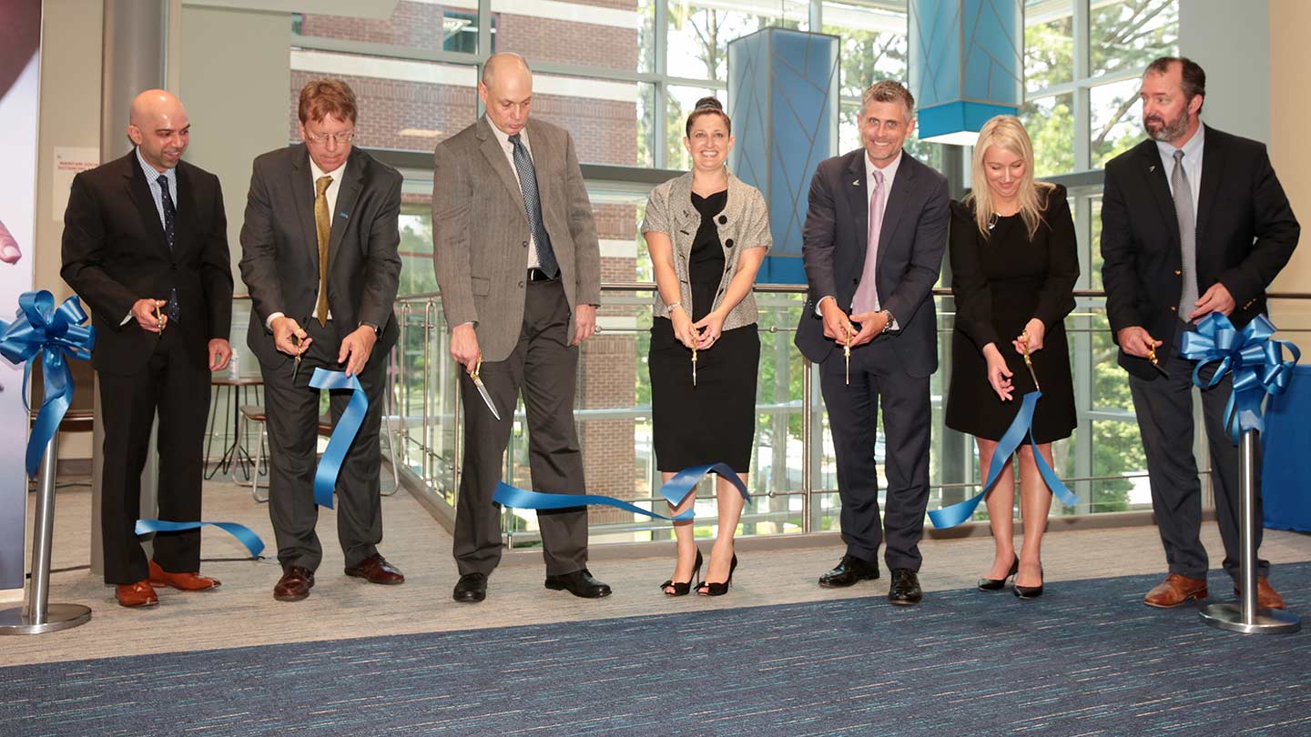 Seven people standing in a line cutting a blue ribbon.