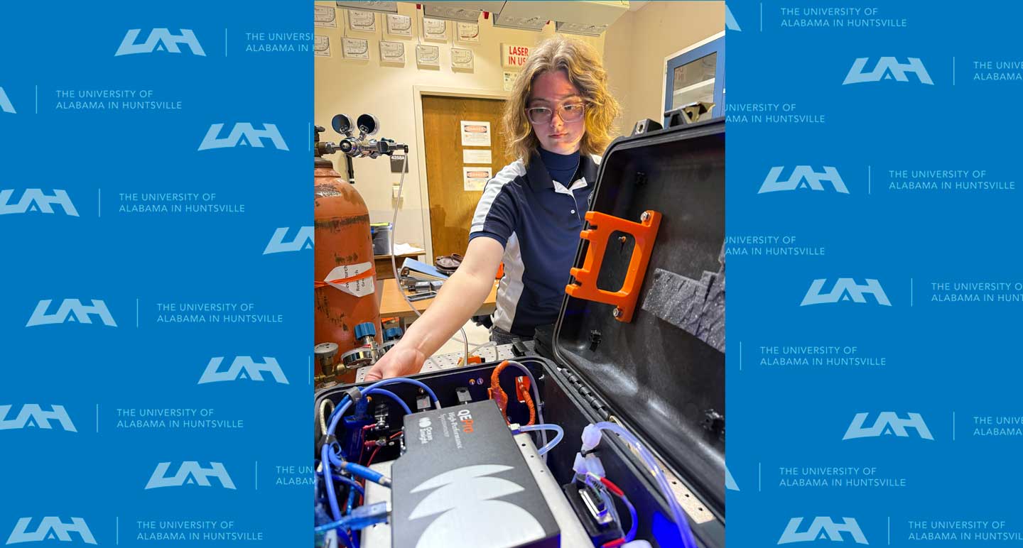 A person holds an open equipment case, displaying various electronic components and wiring, set in a laboratory environment.