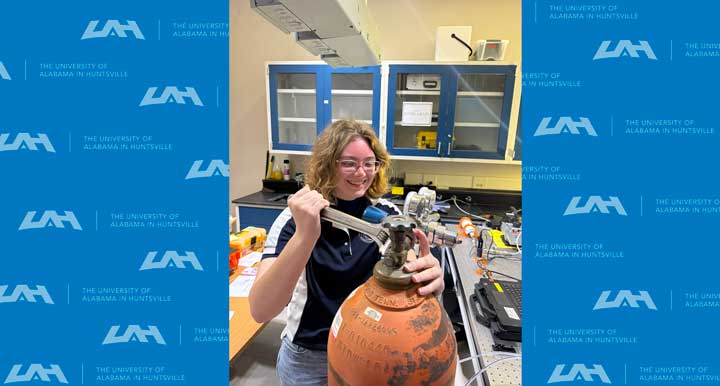 A person works on a gas cylinder in a laboratory setting, surrounded by equipment and blue cabinets.