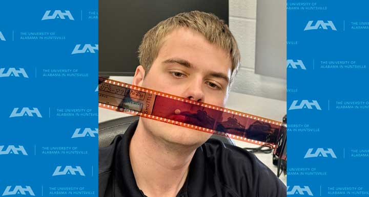 A person is seated in front of a desk with film strips and a backdrop featuring the University of Alabama in Huntsville logo.