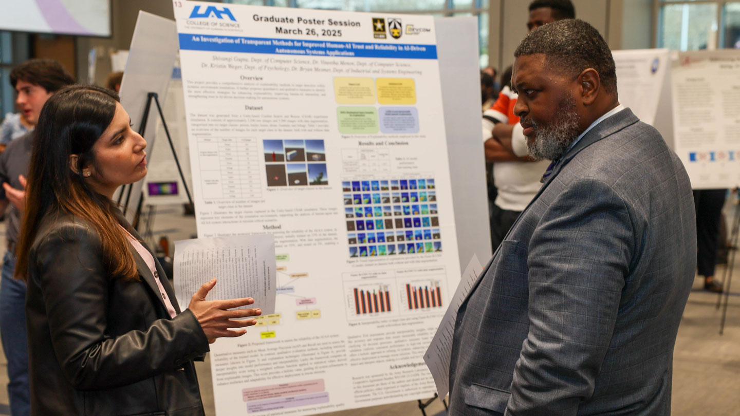 A graduate student discusses their research at a poster session, featuring various charts and visuals about AI methods.