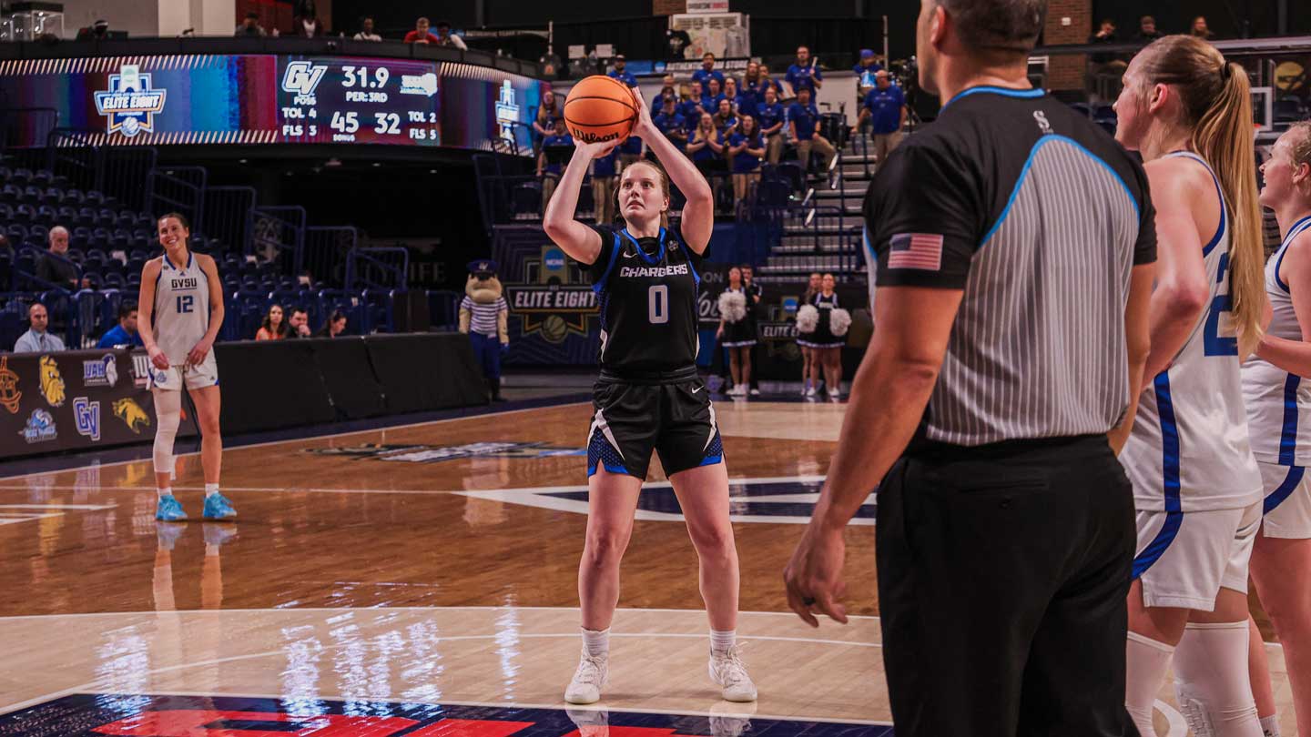Lili Wilken, a basketball player in black uniform prepares to shoot free throw while referee and opposing team watch during game.