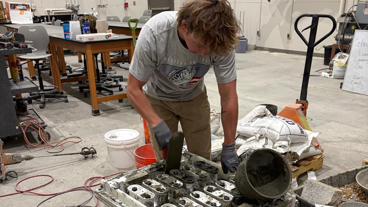 Person in a workshop shoveling concrete into a mold or construction form.