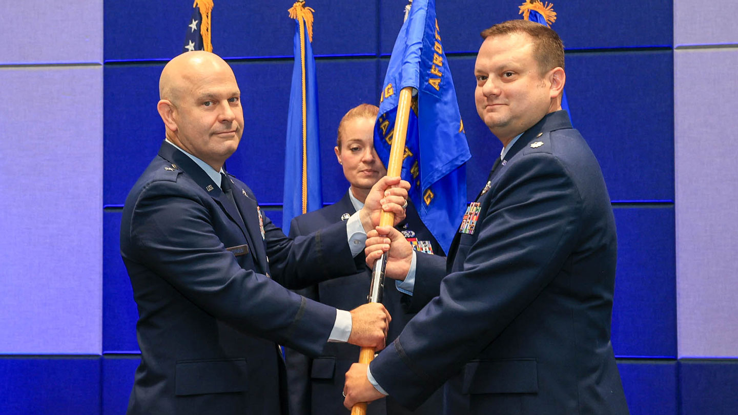 U.S. Air Force Brig. Gen. Joseph Sheffield, left, Jeanne M. Holm Center for Officer Accessions and Citizen Development commander, passes the guidon to Lt. Col. Joseph Johnson, Air Force Reserve Officers’ Training Corps (AFROTC) Detachment 012 commander, as Chief Master Sgt. Jennifer McKeen looks on.