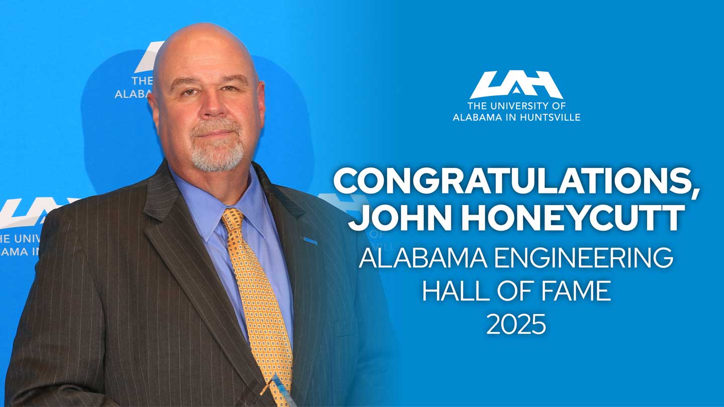 John Honeycutt stands in front of a blue backdrop, holding an award with text congratulating him on his induction into the Alabama Engineering Hall of Fame.