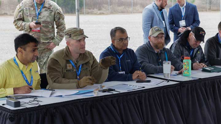 A group of professionals in casual attire seated at a table, engaged in discussion with documents and devices in front of them.