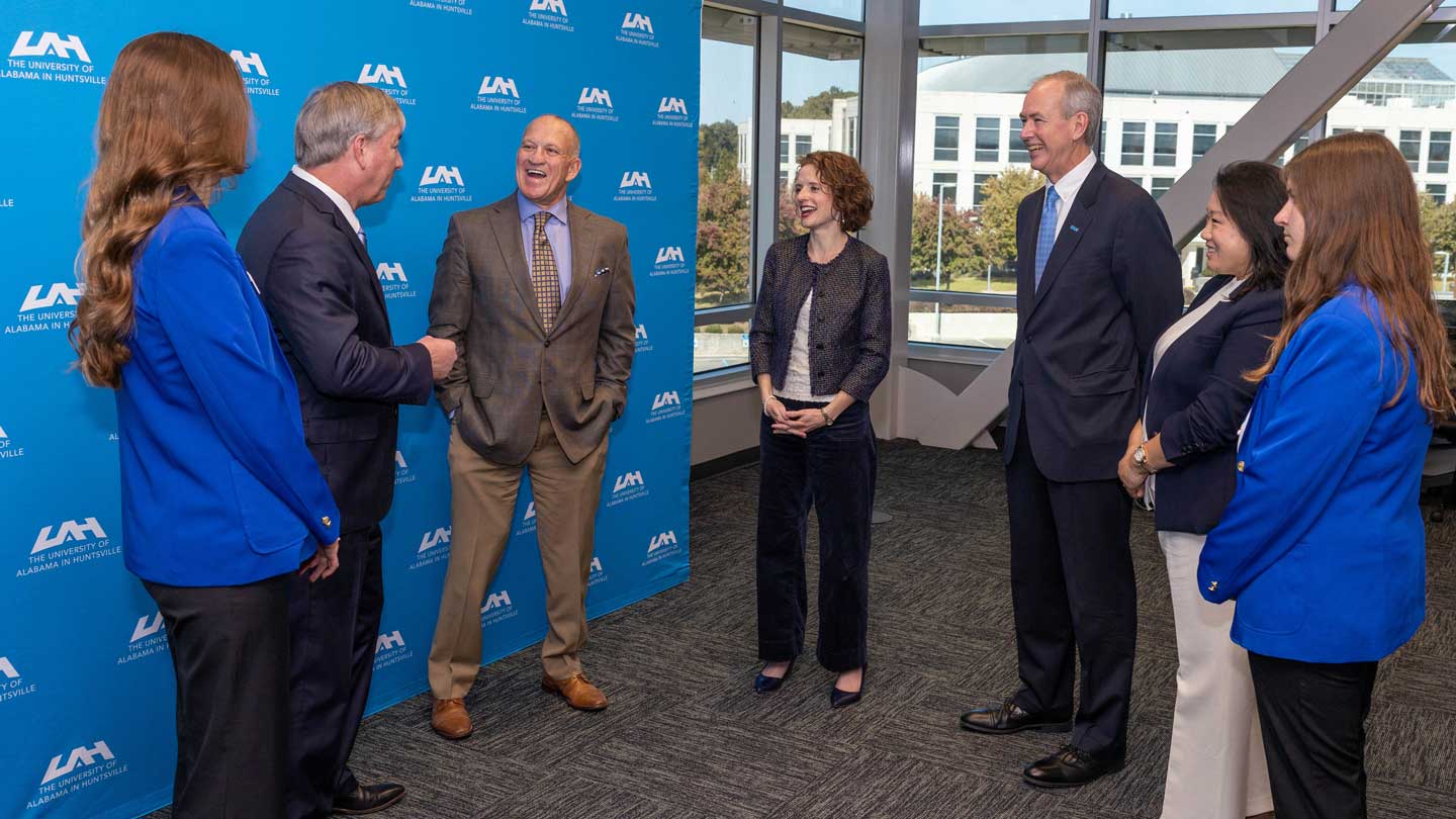 A group of professionals engaged in conversation against UAH banner backdrop, showcasing teamwork and collaboration in a modern setting.