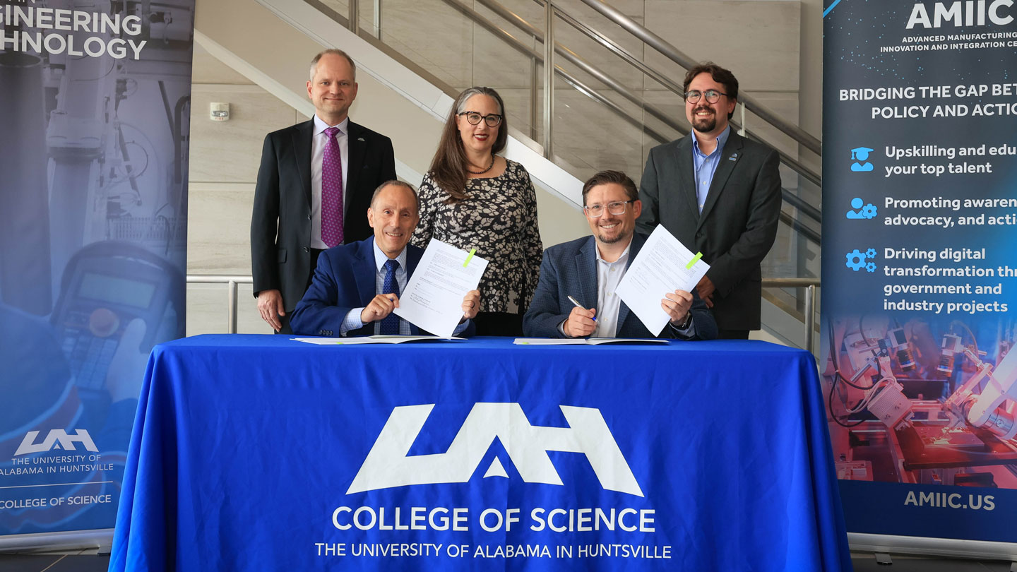 Dr. David A. Puleo, Provost and Executive Vice President for Academic Affairs, and John Schmitt, AMIIC Executive Director (seated). Standing behind them are Dr. Rainer Steinwandt, Dean of the College of Science at UAH, Dr. Alisa Henrie, Assistant Professor and Director of the Engineering Technology program at UAH, and Dr. James Faw, Deputy Director of Laboratory Operations at AMIIC.