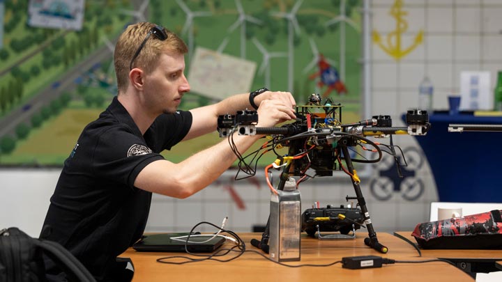 Man adjusting a large quadcopter drone on a workbench indoors.