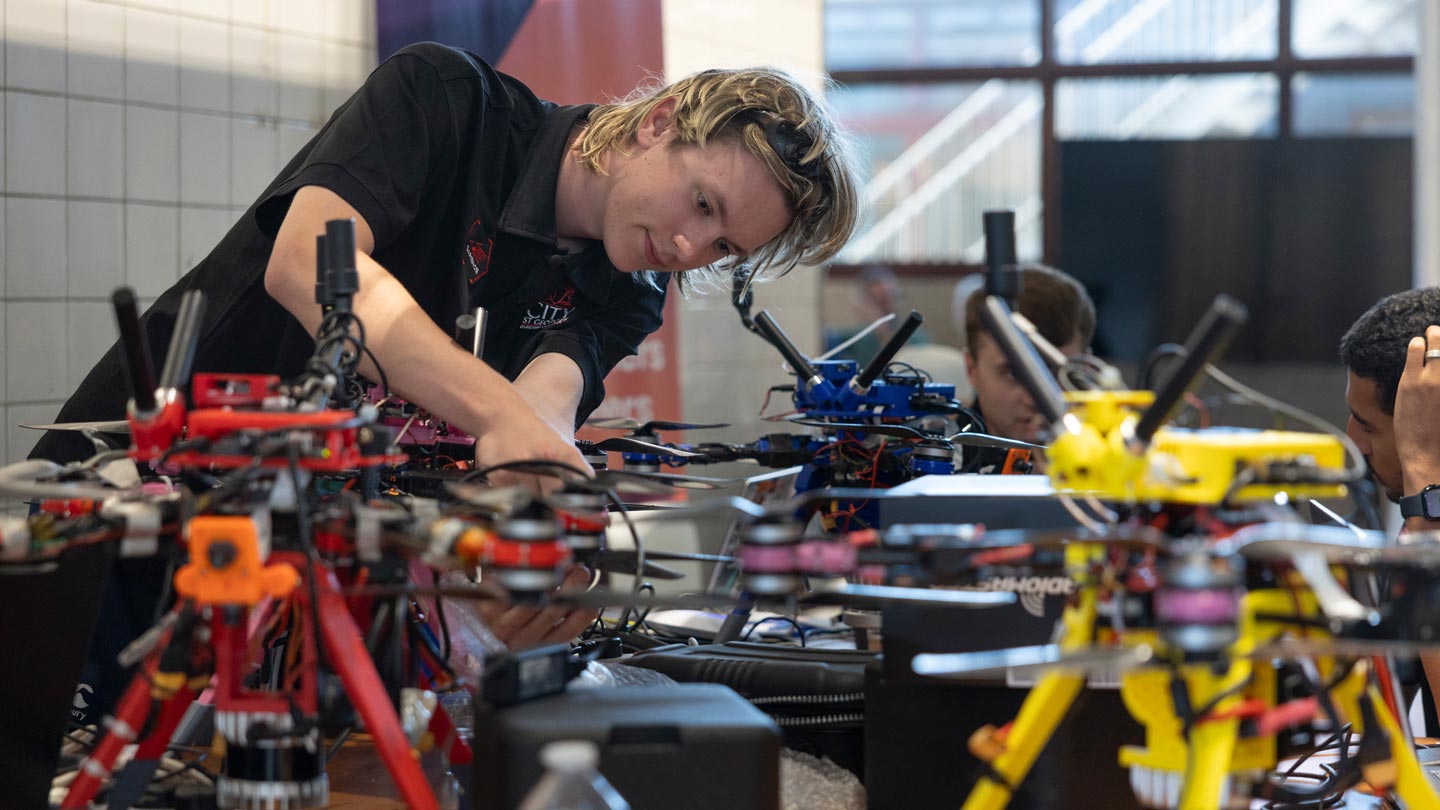 Students in black shirts assemble colorful drones at a robotics workshop.