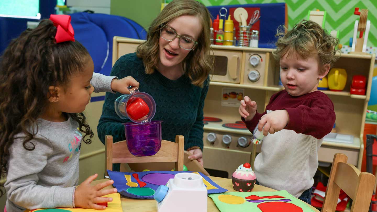 Children engage in imaginative play, pouring colorful liquids and creating with food-shaped toys at a vibrant classroom setting.