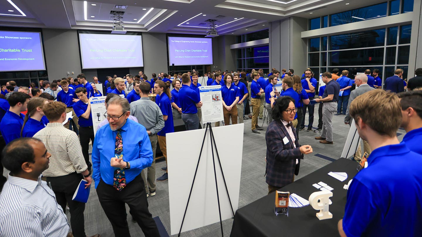 dozens of students in blue pose with presentations and mechanisms