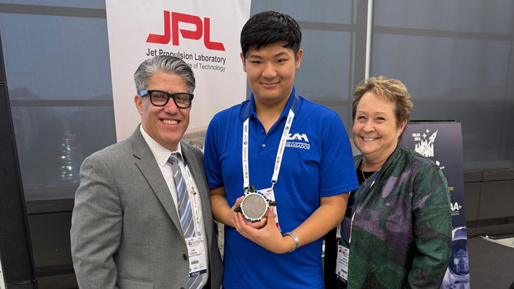 Three individuals standing in front of a JPL banner, middle person holding a SG-2 prototype of gridded ion thruste.