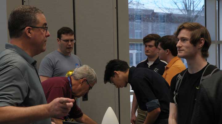 A group of individuals engaged in conversation and activity at the UAH Engineering Expo , with a white display object in the foreground.