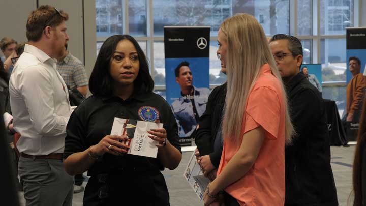 A group of people engages in conversation at the UAH Engineering Expo, with one woman holding a brochure about a program opportunity.