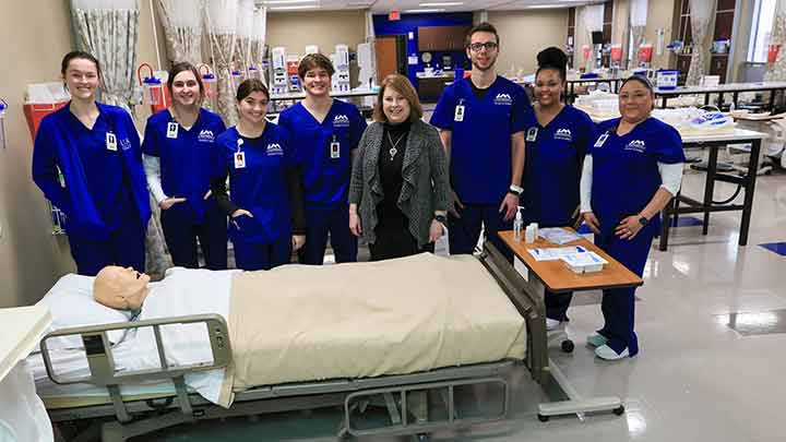 UAH nursing students pose with Dr. Frith in front of a medical testing dummy
