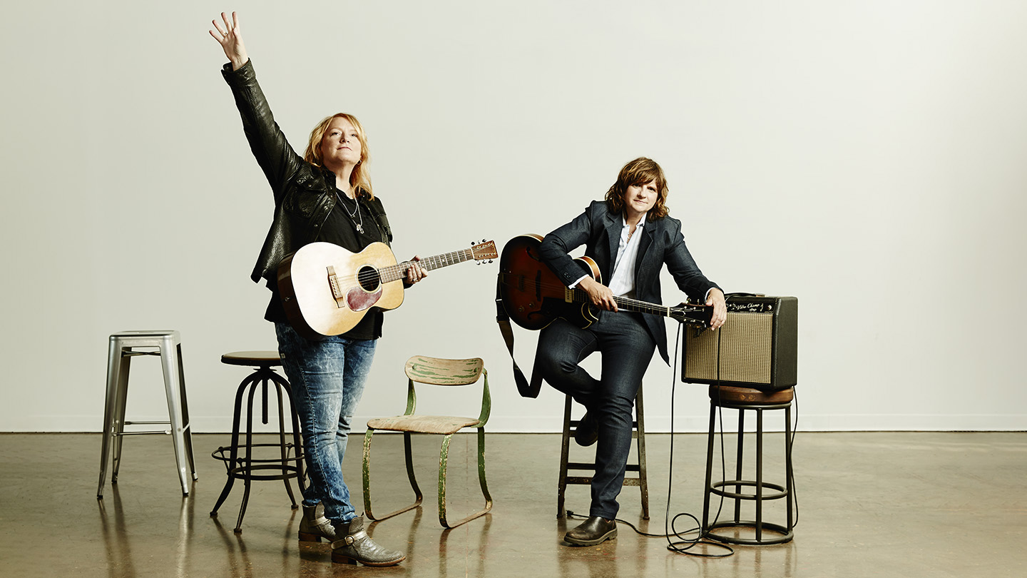 Indigo Girls standing on a stage holding guitars.