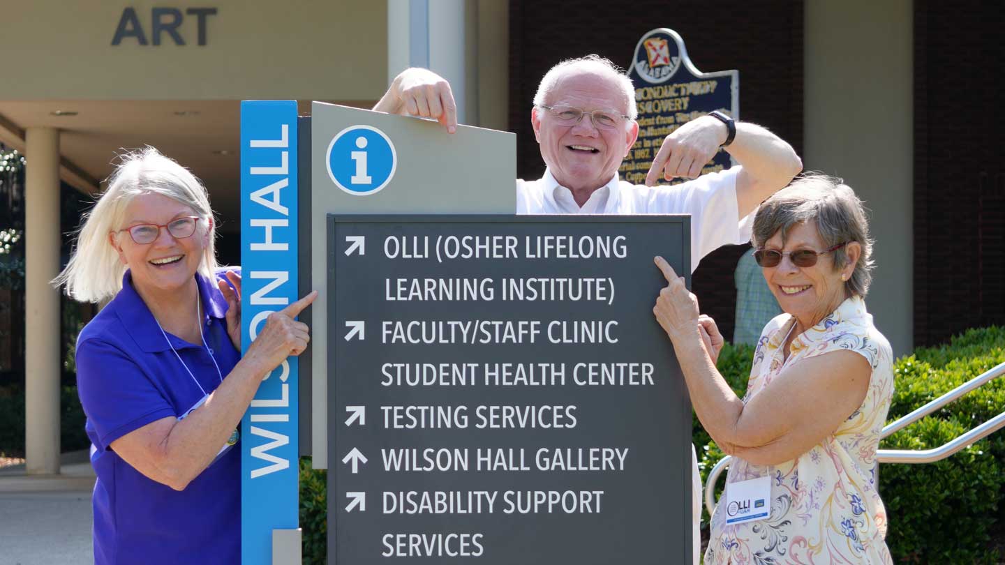 Members of The Osher Lifelong Learning Institute at The University of Alabama in Huntsville, left to right, Marsha Langlois, John Newquist and Sue Chatham – point the way to OLLI’s home in Wilson Hall on the UAH campus.