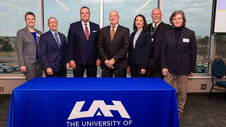 six individuals behind a blue UAH table