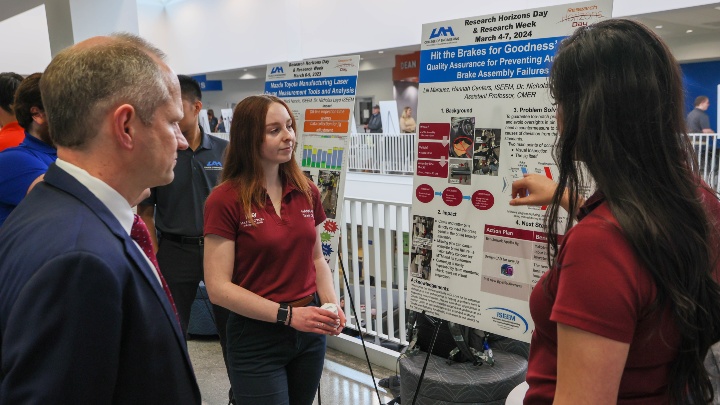 Two female students from The University of Alabama in Huntsville sharing a presentation to a man.