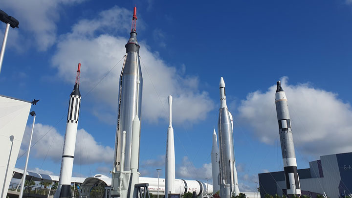Five iconic rockets stand tall against a bright blue sky, showcasing the history of space exploration at a museum.