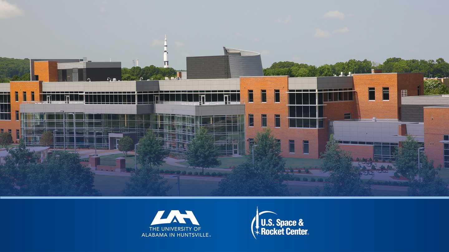  An UAH building with glass and brick architecture, featuring trees and the U.S. Space & Rocket Center in the background.