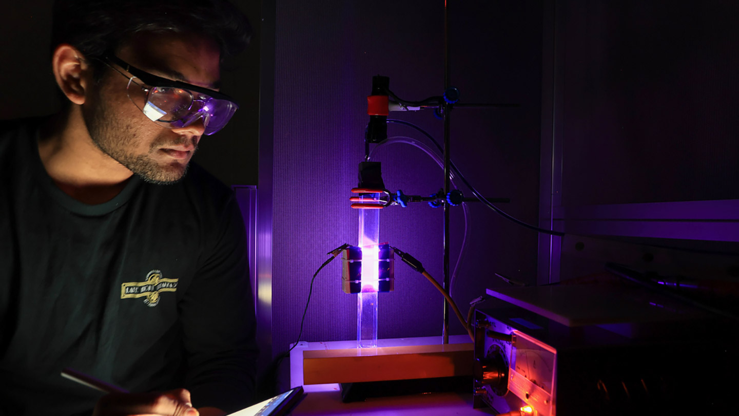 a student in safety glasses takes notes in front of a brightly glowing test tube