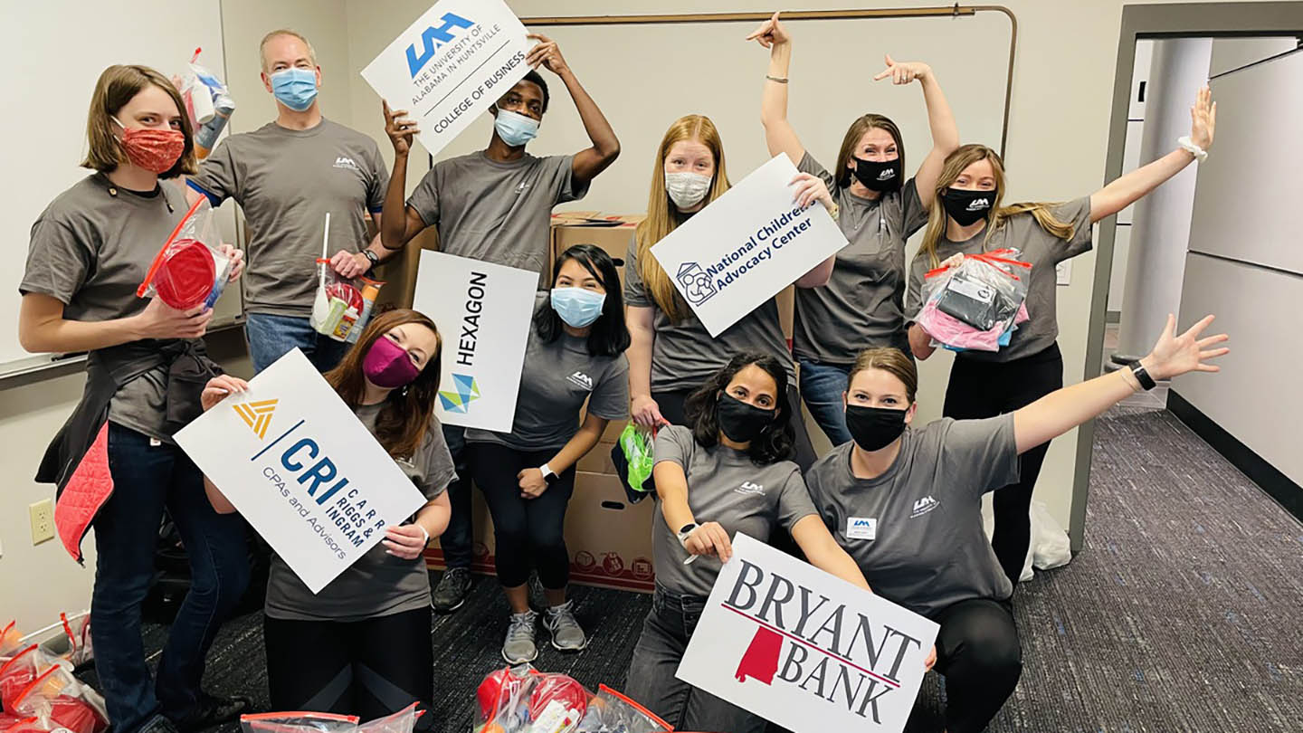 Students pose with sponsor signs after UAH Big Event service day