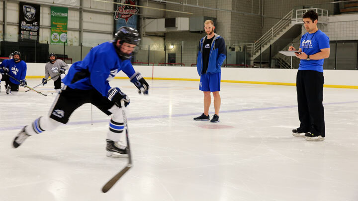 Hockey player on the ice monitored by a coach. ?>