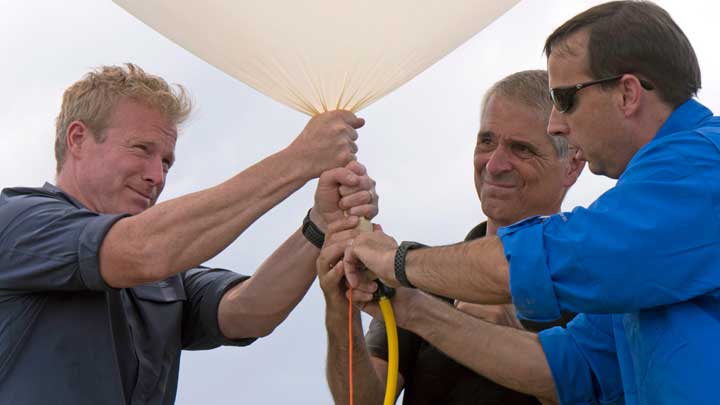 Three people securing an experimental package for launch.