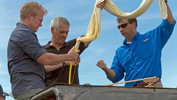 Three people prepare a balloon for launch.