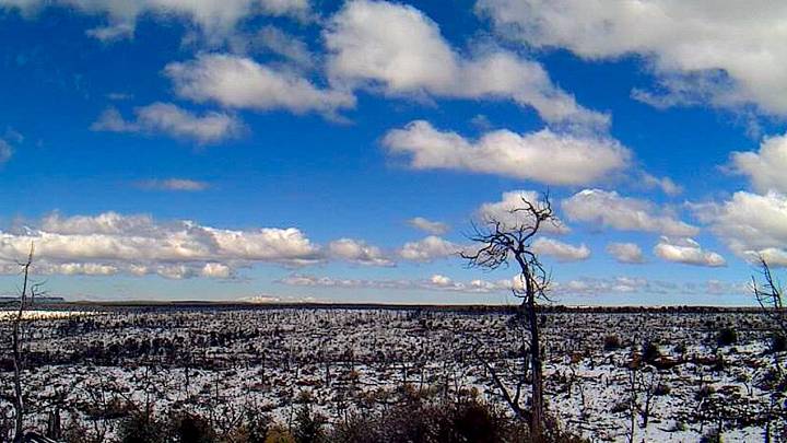 speckled snowy landscape with a partly cloudy blue sky