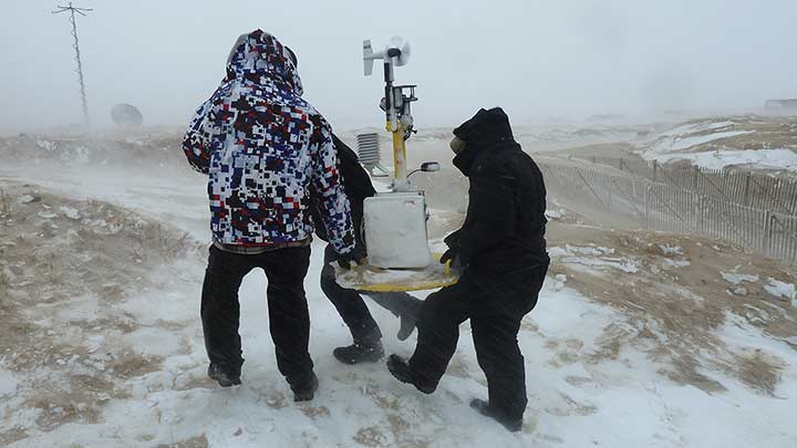 Two people outside in a snowstorm moving equipment.