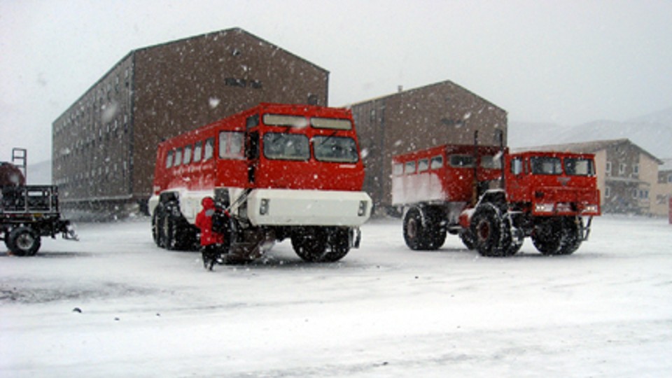 special red buses in the snow in front of large brick buildings